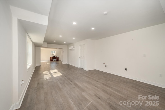 unfurnished living room with recessed lighting, a wall mounted air conditioner, baseboards, and wood finished floors