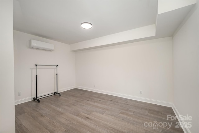 unfurnished room with light wood-style floors, an AC wall unit, and baseboards