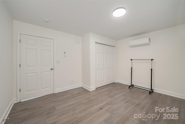 interior space featuring a closet, light wood-type flooring, an AC wall unit, and baseboards