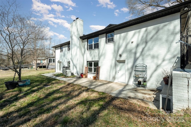 rear view of property with a lawn, ac unit, a chimney, a patio area, and brick siding