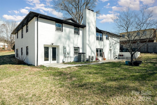 back of property with a patio, brick siding, french doors, a lawn, and a chimney