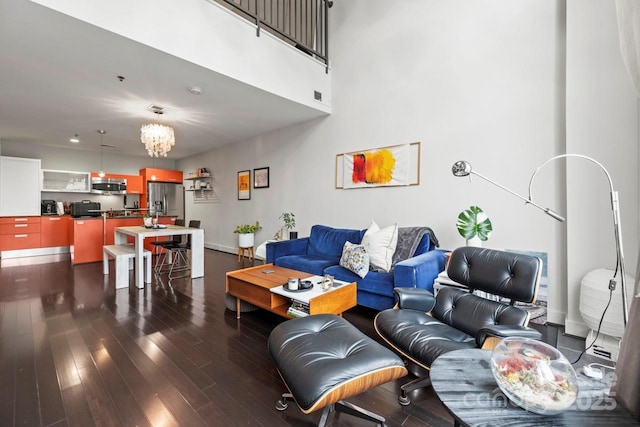 living room featuring a towering ceiling, an inviting chandelier, baseboards, and dark wood-style flooring