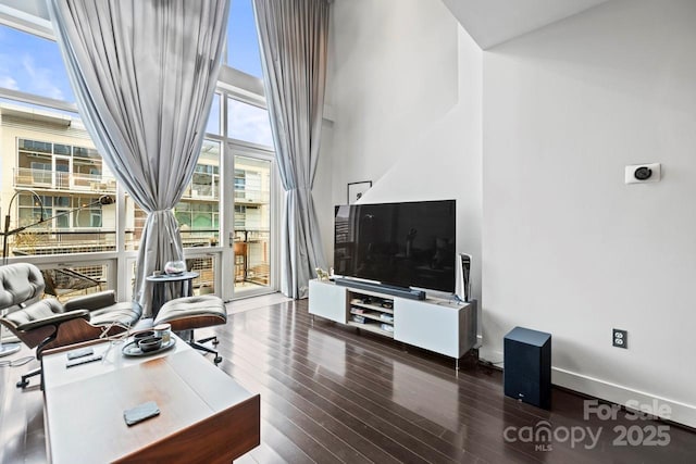 living room featuring wood finished floors, a towering ceiling, and baseboards