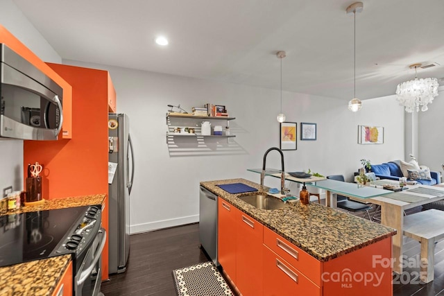 kitchen with a sink, baseboards, appliances with stainless steel finishes, dark stone countertops, and dark wood finished floors