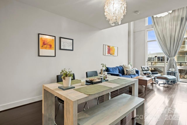 dining space featuring dark wood-style flooring, a notable chandelier, and baseboards