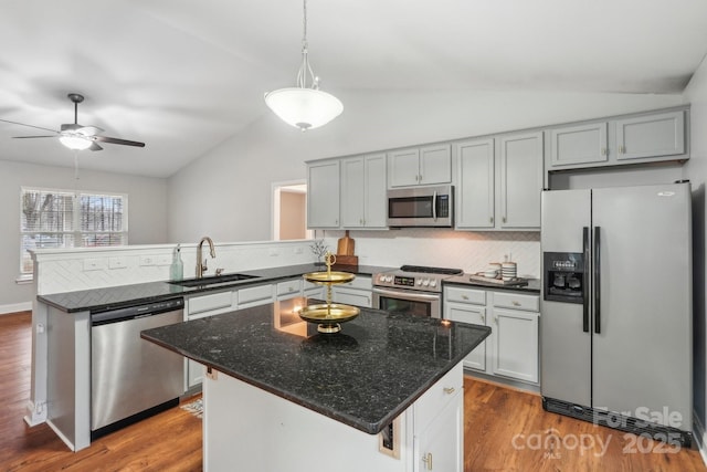 kitchen with appliances with stainless steel finishes, vaulted ceiling, a sink, wood finished floors, and a peninsula