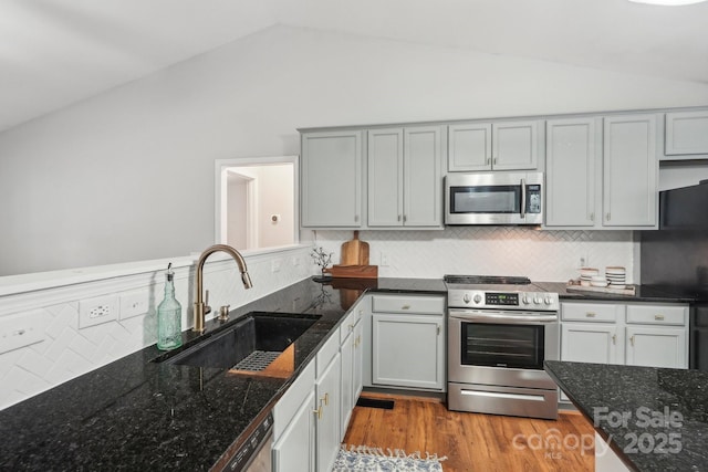 kitchen featuring lofted ceiling, backsplash, appliances with stainless steel finishes, a sink, and wood finished floors