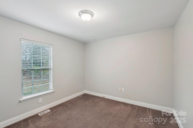 unfurnished room featuring baseboards, visible vents, and dark carpet