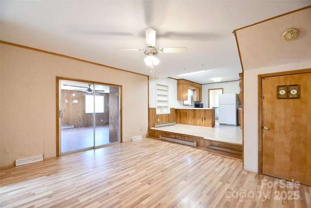 unfurnished living room with ceiling fan, a baseboard heating unit, visible vents, baseboard heating, and light wood-type flooring