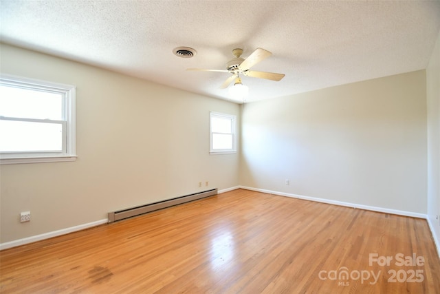 spare room featuring a baseboard heating unit, light wood-type flooring, visible vents, and a textured ceiling