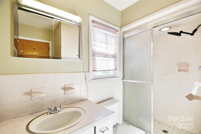 bathroom with toilet, a stall shower, vanity, and tile walls