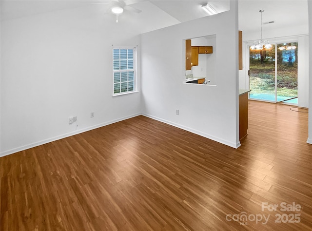 unfurnished living room featuring dark wood-style floors, ceiling fan with notable chandelier, lofted ceiling, and baseboards