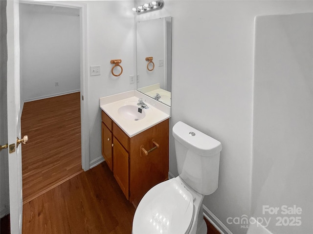 half bathroom featuring toilet, baseboards, wood finished floors, and vanity