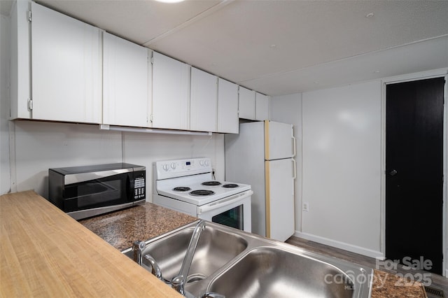 kitchen with white appliances, white cabinets, a sink, and baseboards