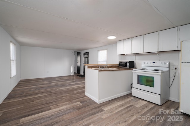 kitchen with white appliances, dark countertops, wood finished floors, and white cabinetry