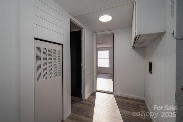 laundry area featuring dark wood-style flooring, a heating unit, cabinet space, and baseboards