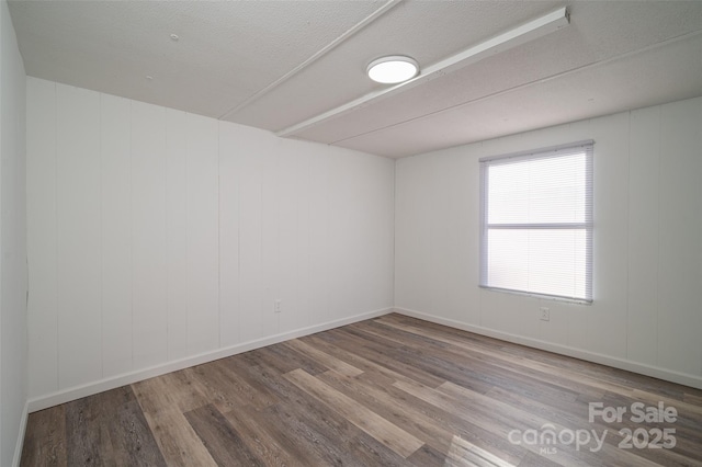 unfurnished room with a textured ceiling, wood finished floors, and baseboards