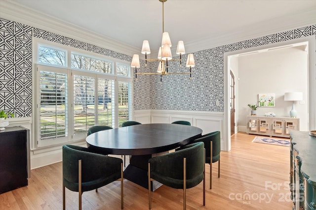 dining space featuring a decorative wall, a wainscoted wall, a notable chandelier, light wood-style floors, and ornamental molding