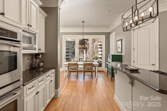 kitchen with appliances with stainless steel finishes, white cabinetry, a notable chandelier, and dark stone countertops