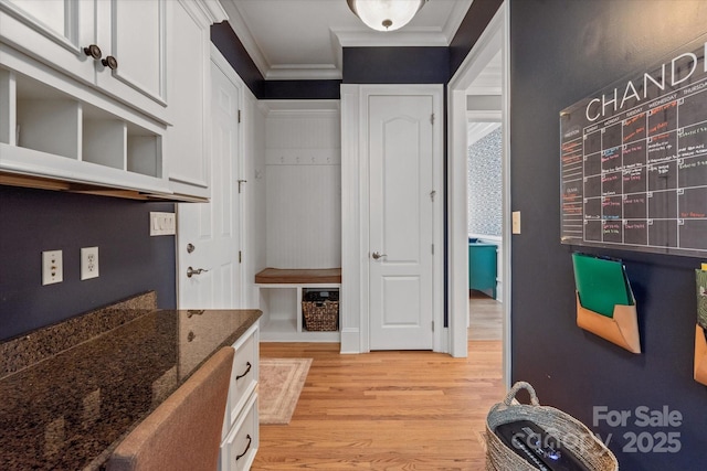 kitchen with light wood-type flooring, white cabinetry, dark stone counters, and crown molding