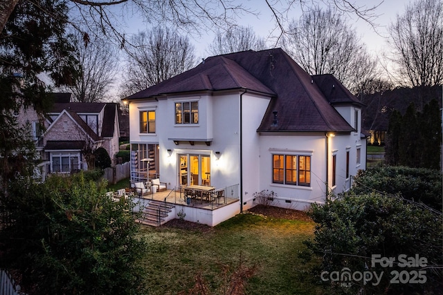 back of property at dusk with a patio, a shingled roof, a yard, crawl space, and stucco siding