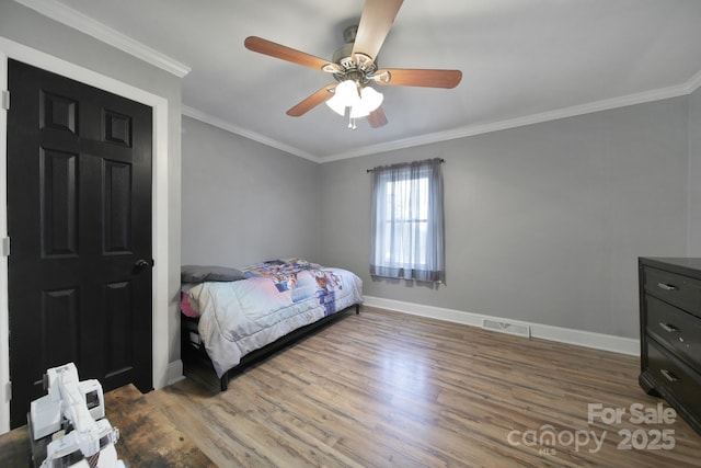 bedroom with ornamental molding, visible vents, baseboards, and wood finished floors