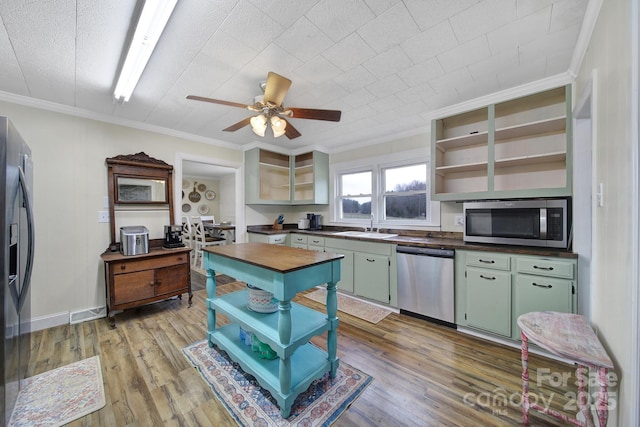 kitchen featuring stainless steel appliances, wood finished floors, a sink, ornamental molding, and open shelves