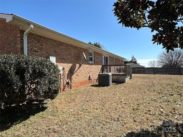 view of side of home featuring a deck, central air condition unit, brick siding, fence, and a lawn