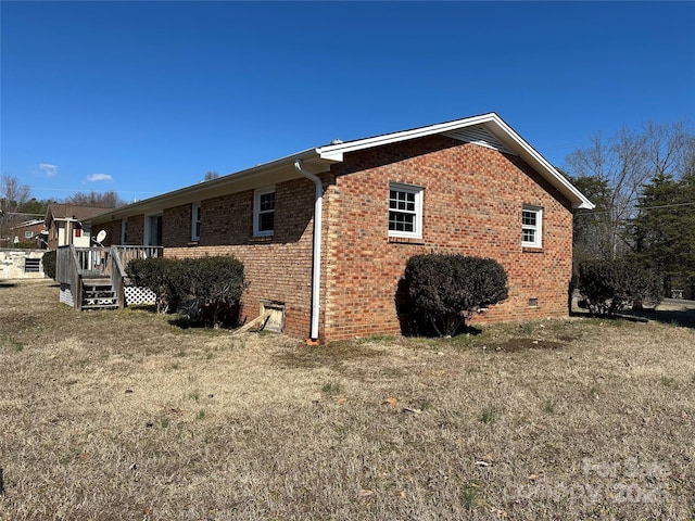 view of property exterior with crawl space, a wooden deck, a lawn, and brick siding