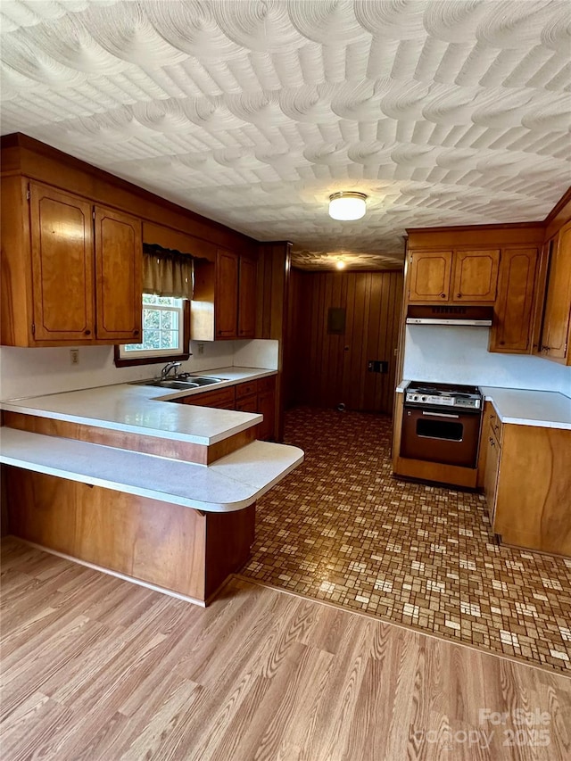 kitchen featuring a peninsula, brown cabinetry, range, and light countertops