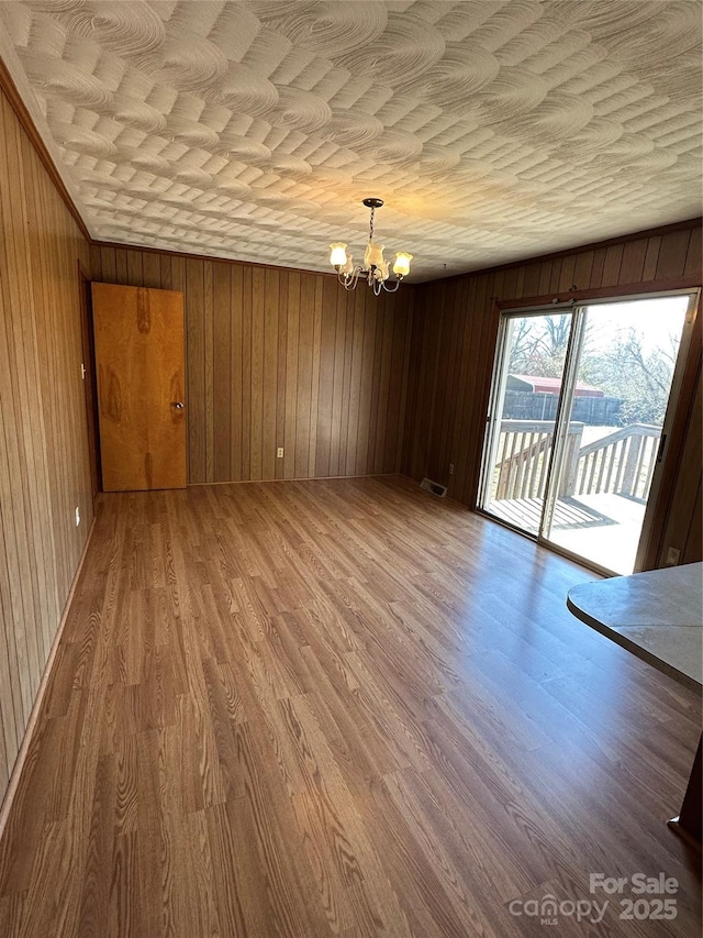 interior space with a chandelier, visible vents, wood walls, and wood finished floors