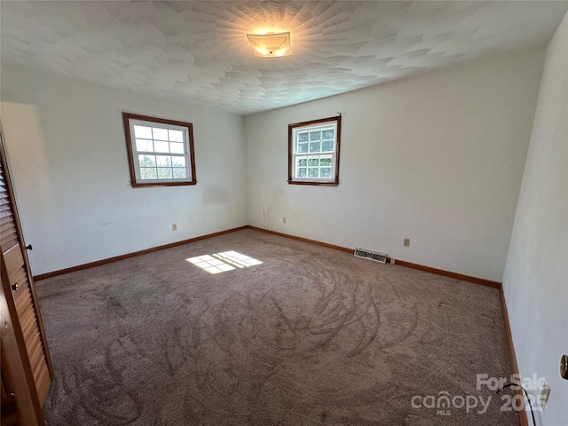 carpeted empty room with baseboards, a textured ceiling, visible vents, and a wealth of natural light