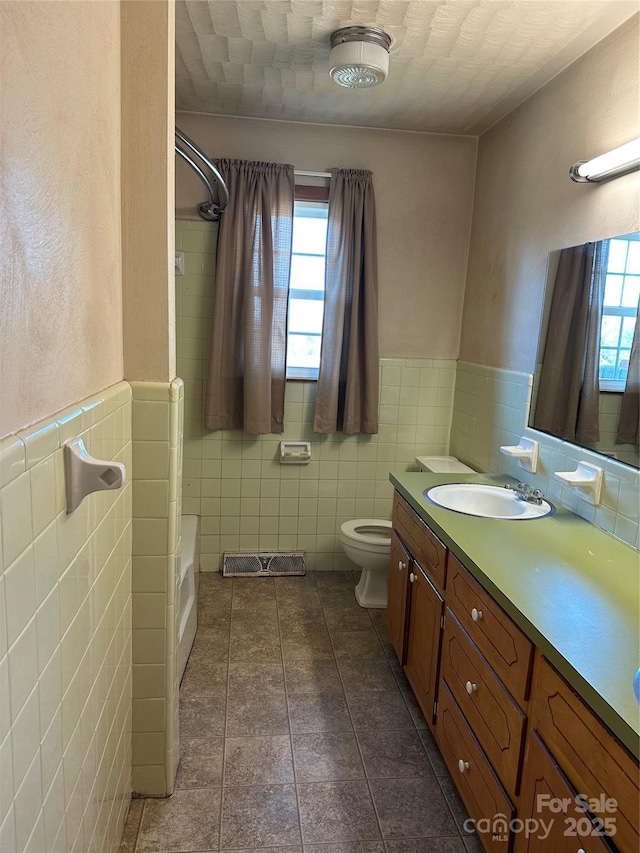 full bath featuring toilet, a wainscoted wall, tile patterned flooring, vanity, and tile walls