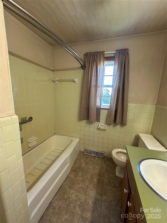 full bath with toilet, a wainscoted wall, bathtub / shower combination, vanity, and tile walls