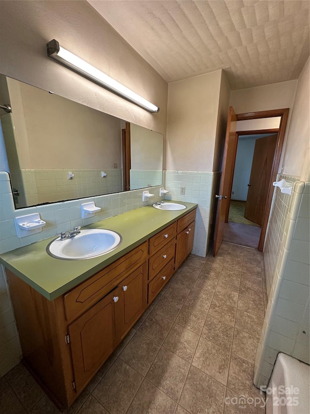 bathroom featuring a wainscoted wall, double vanity, a sink, and tile walls