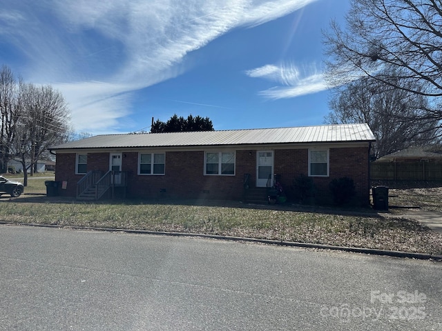 ranch-style house with brick siding, metal roof, and a front lawn