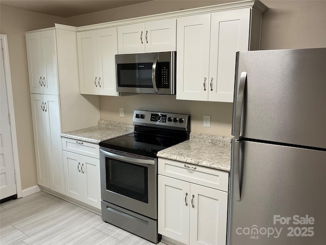 kitchen with appliances with stainless steel finishes, light wood-type flooring, light stone countertops, and white cabinets