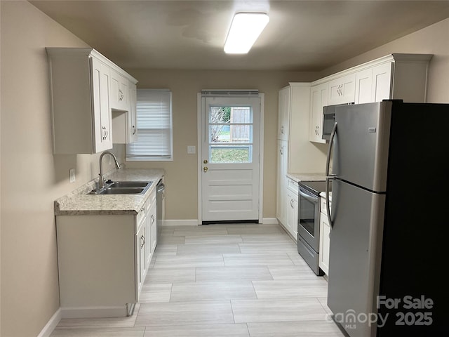 kitchen featuring a sink, white cabinetry, baseboards, light countertops, and appliances with stainless steel finishes