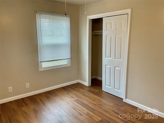 unfurnished bedroom with a closet, wood finished floors, and baseboards