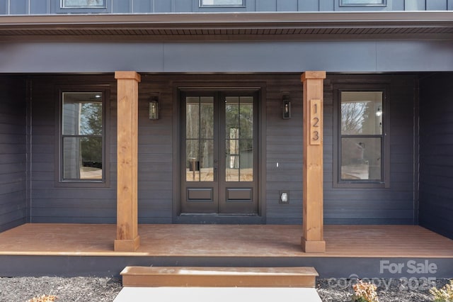 view of exterior entry with covered porch, french doors, and board and batten siding