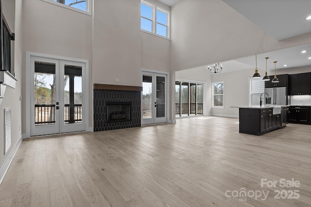 unfurnished living room with a fireplace, a sink, french doors, light wood-type flooring, and an inviting chandelier