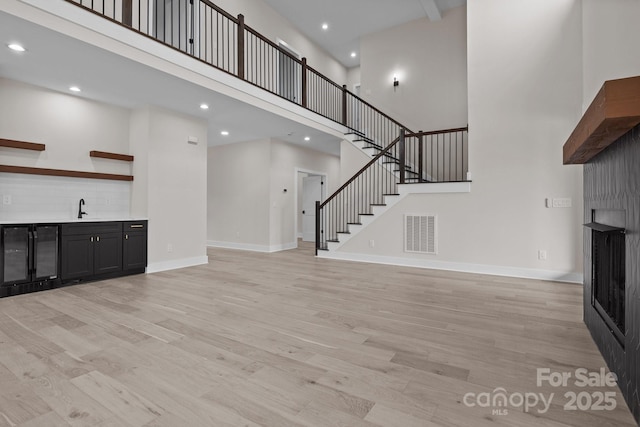 unfurnished living room featuring light wood-style flooring, stairs, visible vents, and baseboards