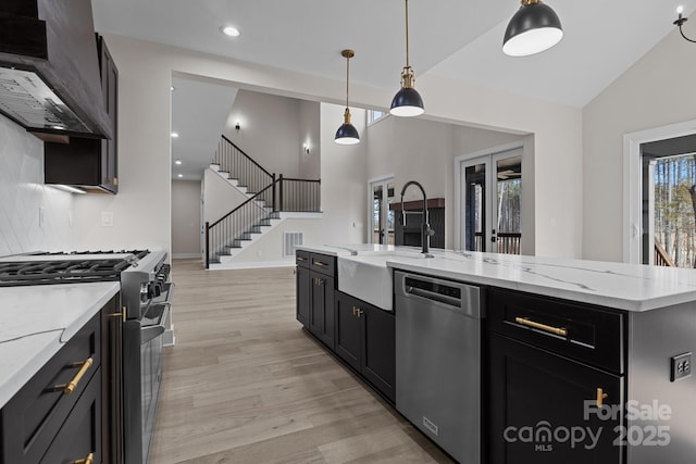 kitchen featuring appliances with stainless steel finishes, pendant lighting, dark cabinetry, and light wood-style floors