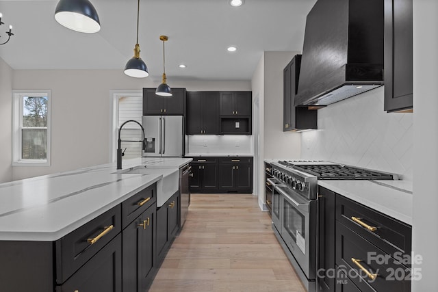 kitchen with dark cabinets, a sink, hanging light fixtures, appliances with stainless steel finishes, and custom range hood