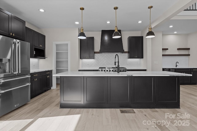 kitchen with decorative light fixtures, open shelves, high end fridge, light countertops, and a kitchen island with sink