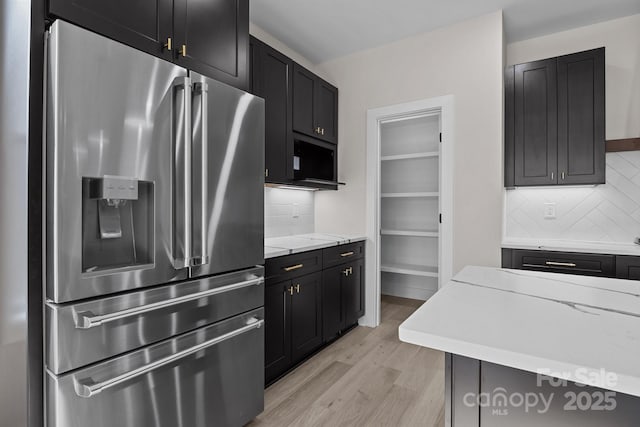 kitchen with tasteful backsplash, high end fridge, dark cabinetry, and light wood finished floors