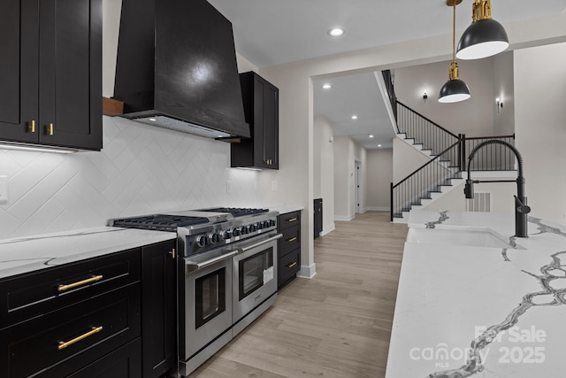 kitchen with range with two ovens, light wood-style flooring, dark cabinets, custom range hood, and pendant lighting