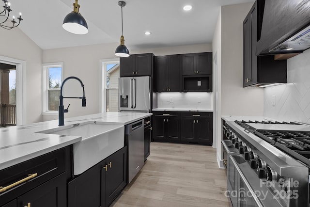 kitchen featuring premium appliances, decorative light fixtures, light wood finished floors, a sink, and dark cabinetry