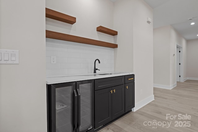 bar featuring tasteful backsplash, light wood-style floors, a sink, beverage cooler, and baseboards