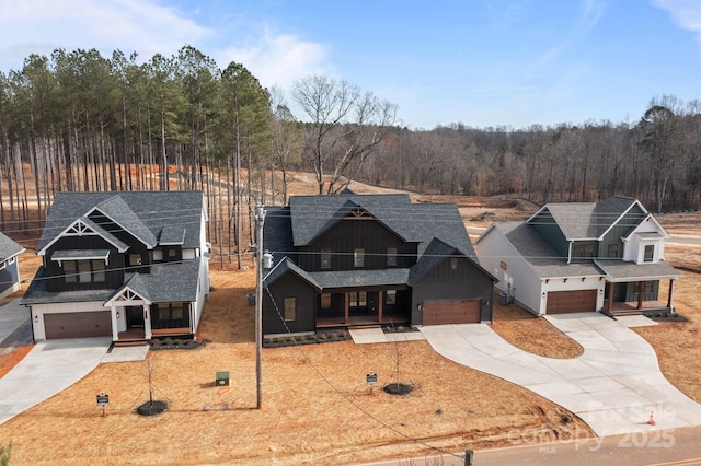 view of front facade with a garage, concrete driveway, a shingled roof, and a forest view